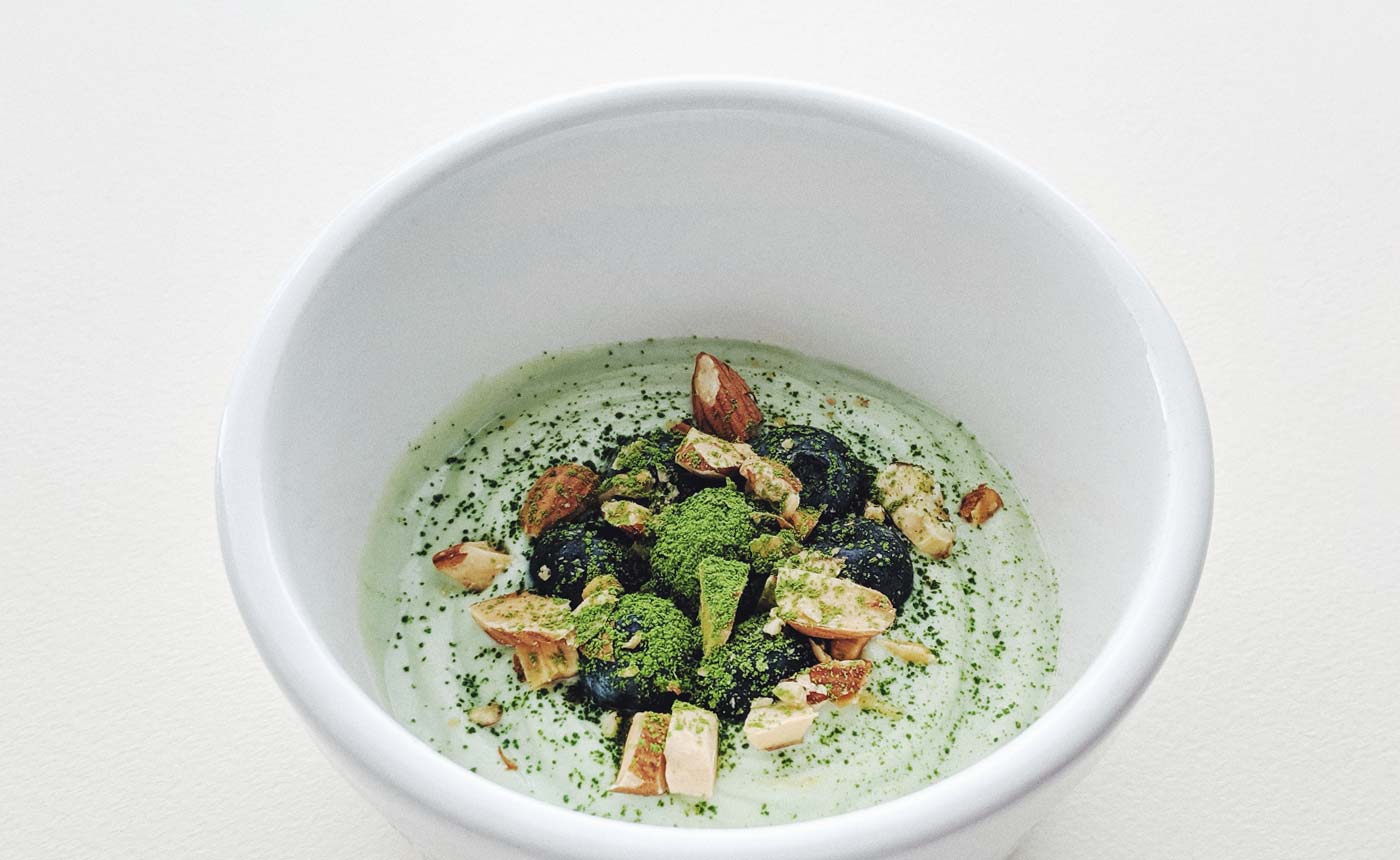 a dish garnished with blue berries, nuts, and matcha green tea