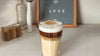 Hojicha latte on a table in front of a sign reading,
