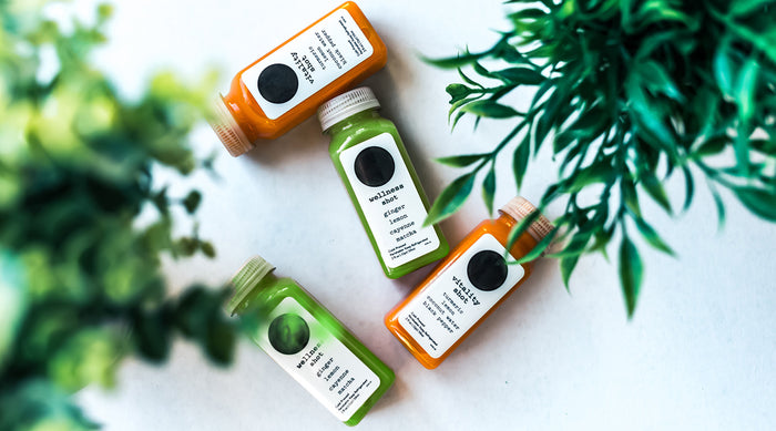 Plastic bottles of matcha and carrot juice on white background with leaves in the foreground.