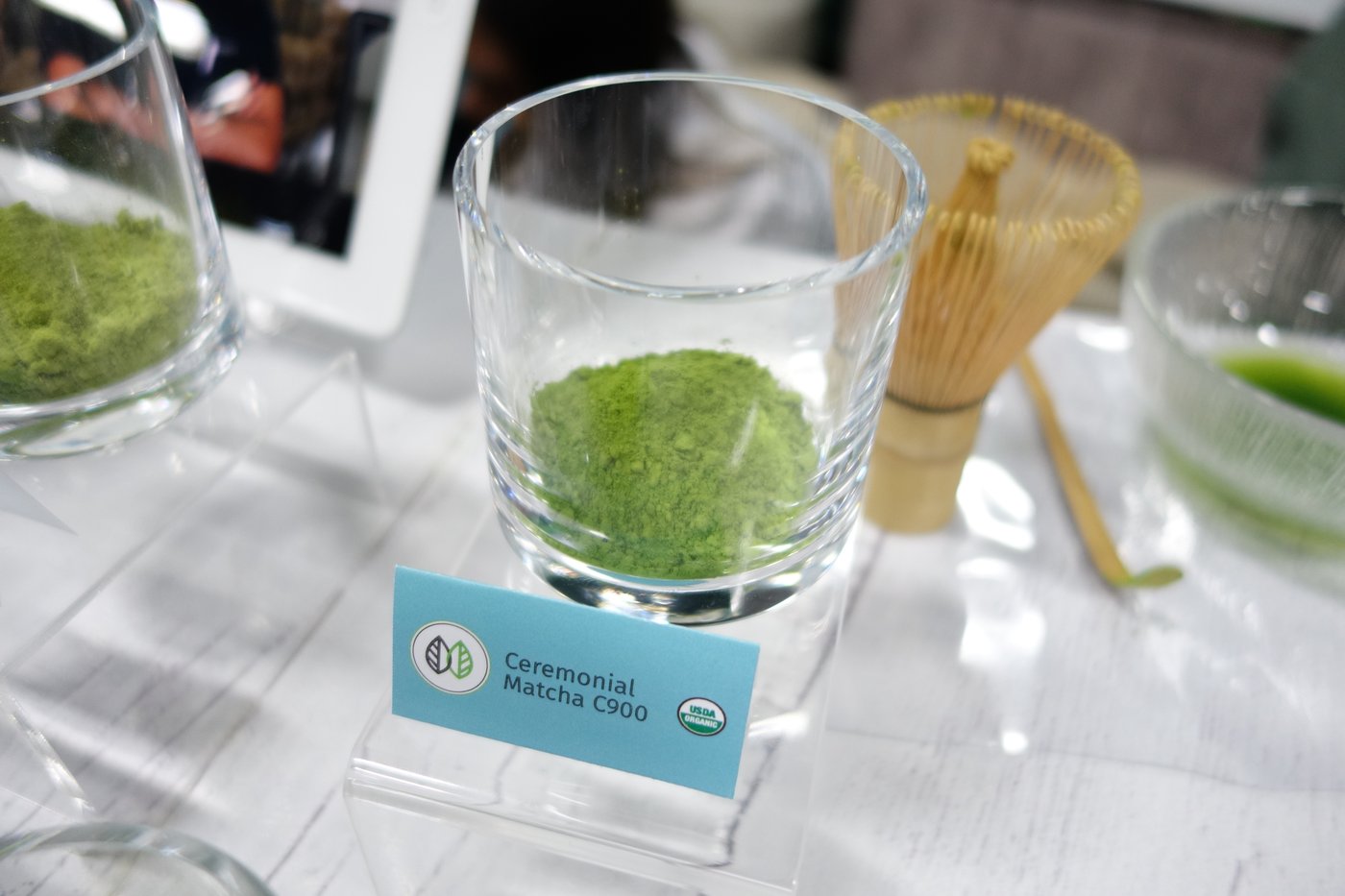 Ceremonial matcha in a glass cup in front of a chasen whisk and chashaku