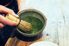 matcha being whisked in a bowl over a wooden table surface