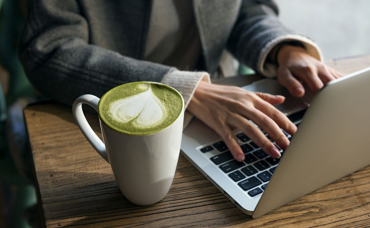 a matcha latte next to a person working at a laptop