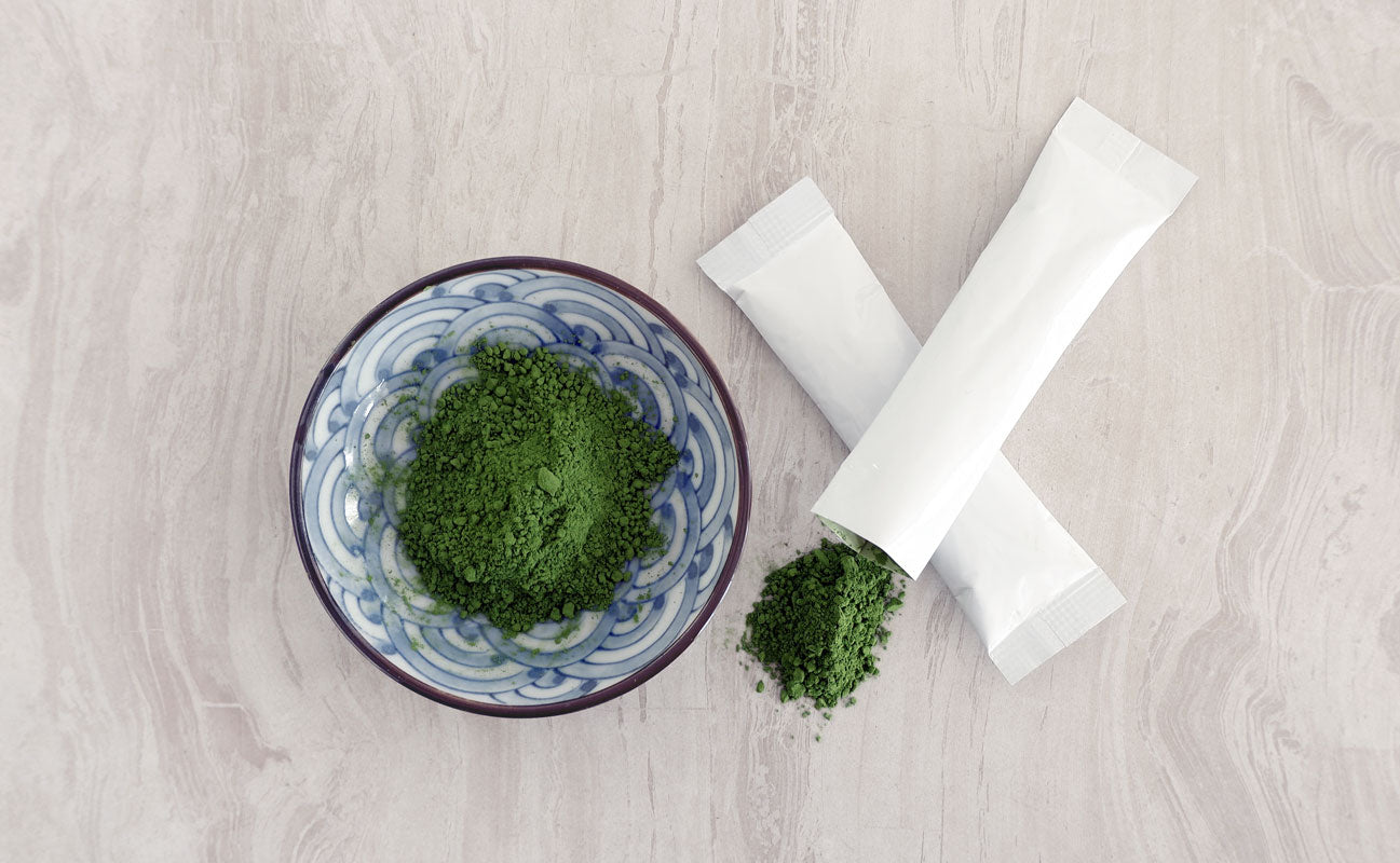 matcha stick packs next to a small, blue bowl of matcha on a white surface