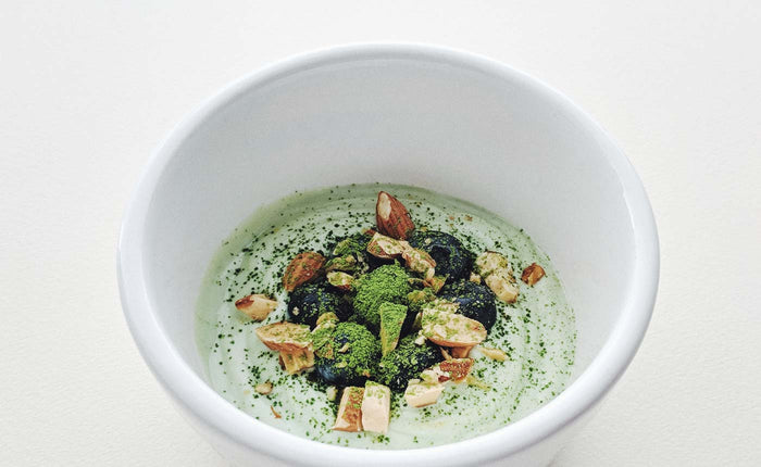 a dish garnished with blue berries, nuts, and matcha green tea